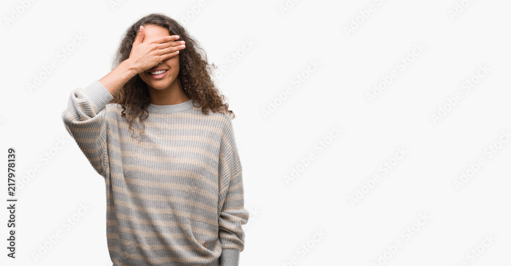 Beautiful young hispanic woman wearing stripes sweater smiling and laughing with hand on face covering eyes for surprise. Blind concept. Beautiful young hispanic woman wearing stripes sweater smiling and laughing with hand on face covering eyes for surprise. Blind concept.