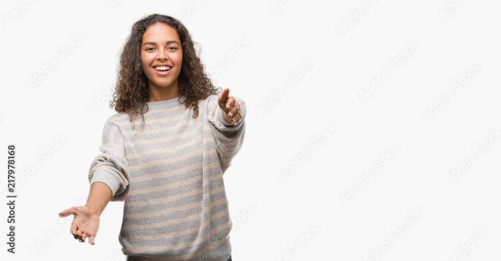 Beautiful young hispanic woman wearing stripes sweater looking at the camera smiling with open arms for hug. Cheerful expression embracing happiness. Beautiful young hispanic woman wearing stripes sweater looking at the camera smiling with open arms for hug. Cheerful expression embracing happiness.