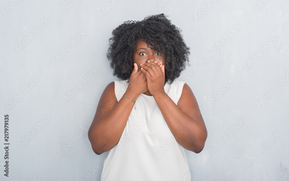 Young african american woman over grey grunge wall shocked covering mouth with hands for mistake. Secret concept. Young african american woman over grey grunge wall shocked covering mouth with hands for mistake. Secret concept.