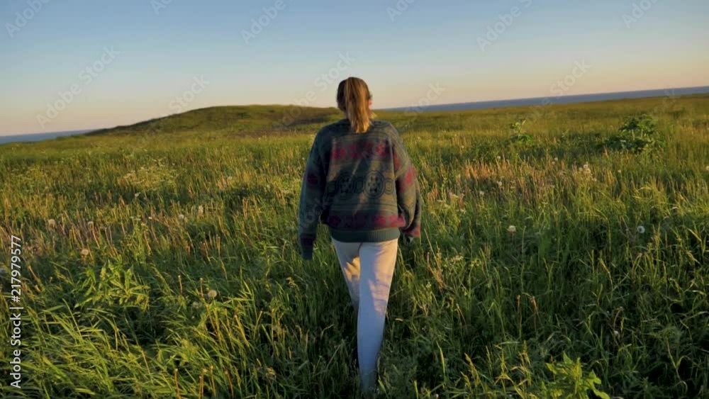 A young woman walking through a field of tall grass toward the sea. Slow motion, MEDIUM WIDE, FOLLOW SHOT. A young woman walking through a field of tall grass toward the sea. Slow motion, MEDIUM WIDE, FOLLOW SHOT.