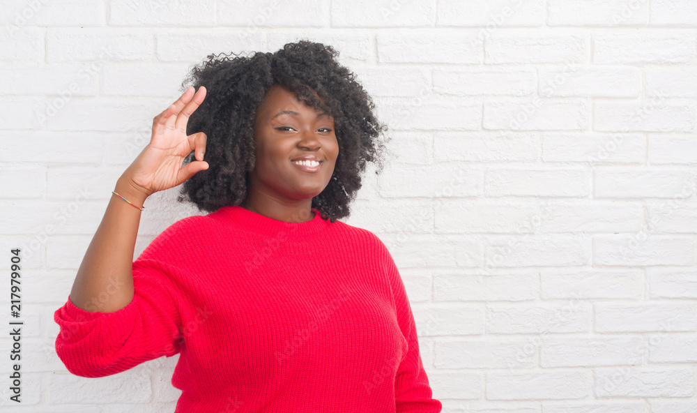 Young african american plus size woman over white brick wall smiling positive doing ok sign with hand and fingers. Successful expression. Young african american plus size woman over white brick wall smiling positive doing ok sign with hand and fingers. Successful expression.