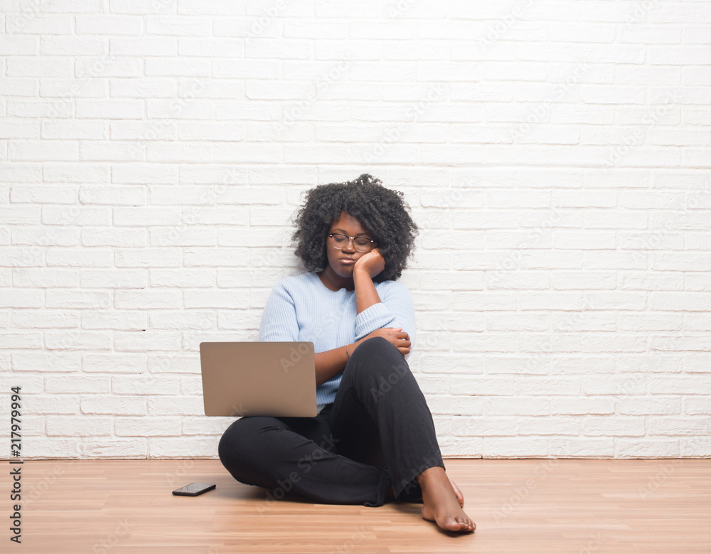 Young african american woman sitting on the floor using laptop at home thinking looking tired and bored with depression problems with crossed arms. Young african american woman sitting on the floor using laptop at home thinking looking tired and bored with depression problems with crossed arms.