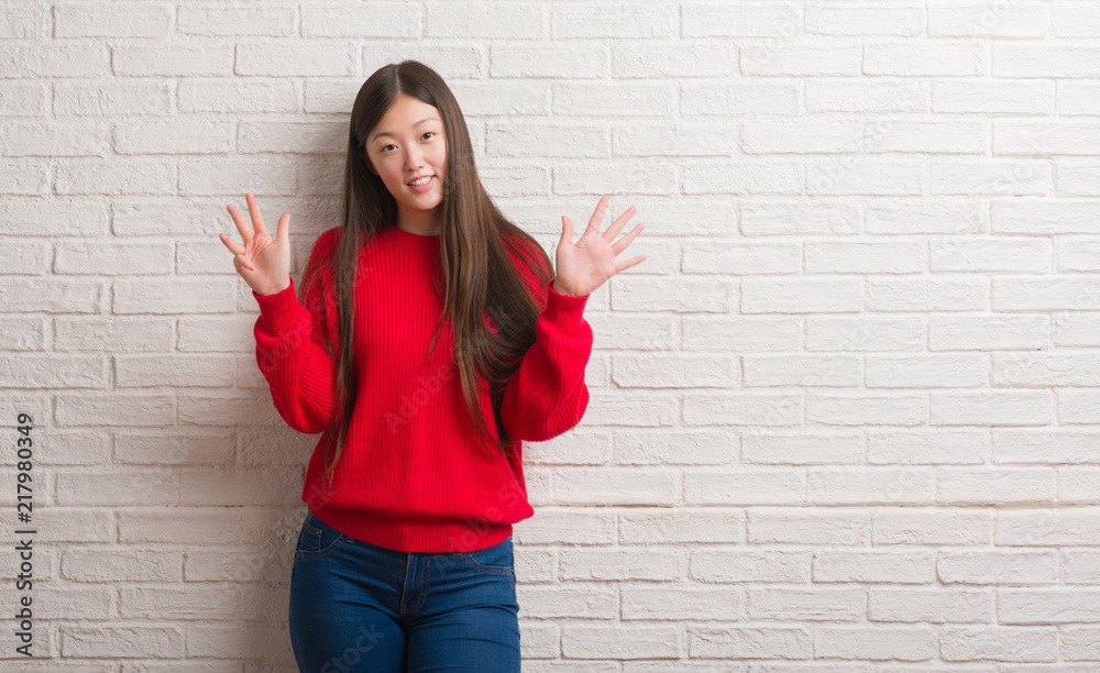 Young Chinese woman over brick wall showing and pointing up with fingers number nine while smiling confident and happy. Young Chinese woman over brick wall showing and pointing up with fingers number nine while smiling confident and happy.