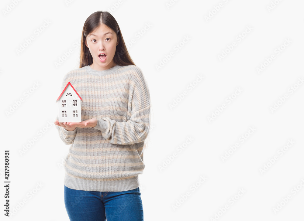 Young Chinese real state agent woman over isolated background holding house scared in shock with a surprise face, afraid and excited with fear expression Young Chinese real state agent woman over isolated background holding house scared in shock with a surprise face, afraid and excited with fear expression