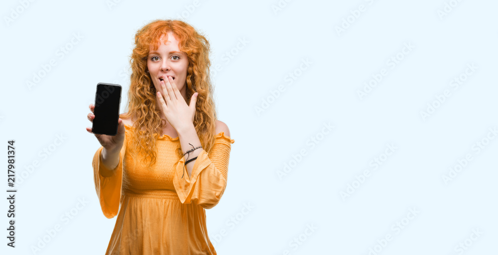 Young redhead woman showing smartphone cover mouth with hand shocked with shame for mistake, expression of fear, scared in silence, secret concept