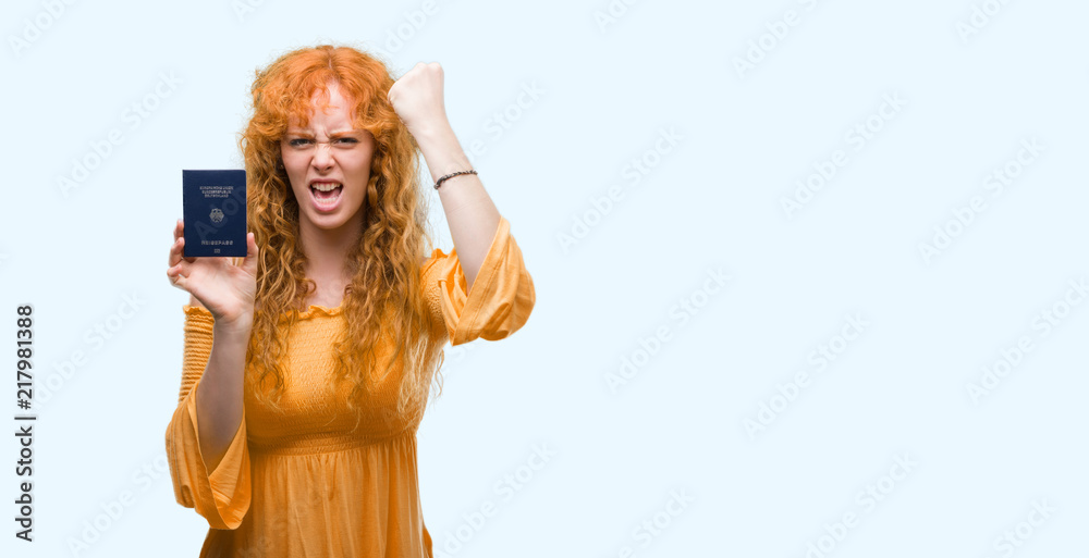 Young redhead woman holding passport of Germany annoyed and frustrated shouting with anger, crazy and yelling with raised hand, anger concept