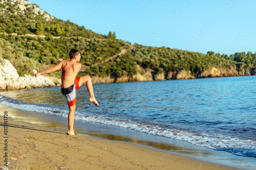Boy on sand shoots the ball into the blue sea Boy on sand shoots the ball into the blue sea