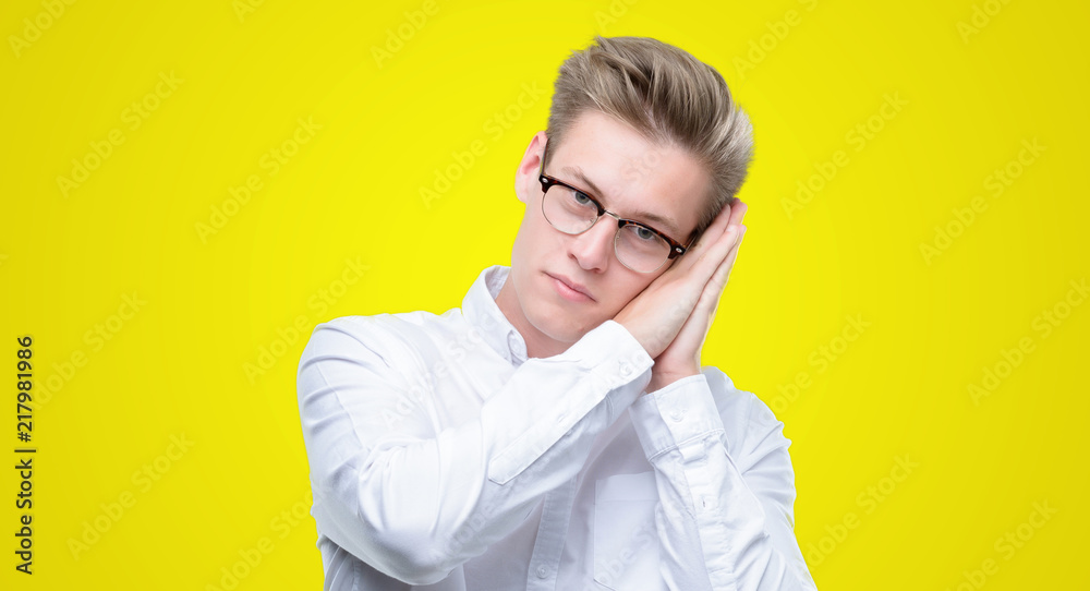 Young handsome blond man sleeping tired dreaming and posing with hands together while smiling with closed eyes. Young handsome blond man sleeping tired dreaming and posing with hands together while smiling with closed eyes.