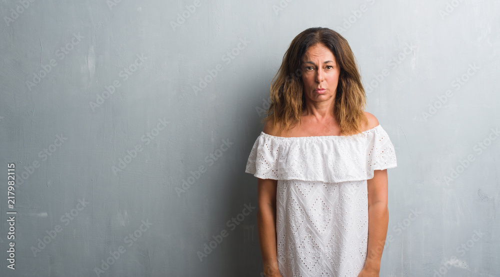 Middle age hispanic woman standing over grey grunge wall depressed and worry for distress, crying angry and afraid. Sad expression. Middle age hispanic woman standing over grey grunge wall depressed and worry for distress, crying angry and afraid. Sad expression.