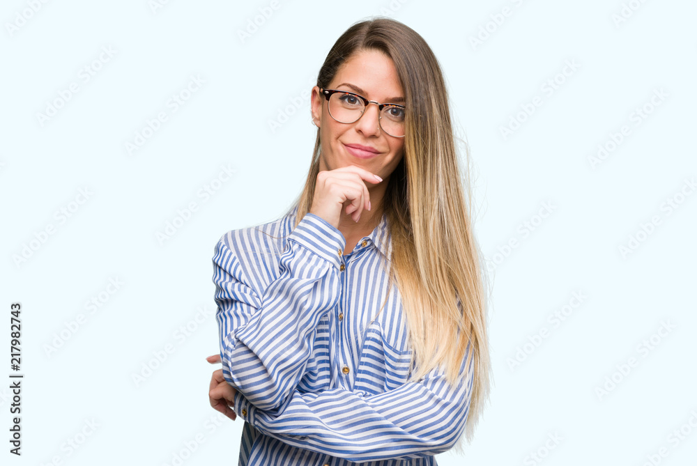 Beautiful young woman wearing elegant shirt and glasses looking confident at the camera with smile with crossed arms and hand raised on chin. Thinking positive.