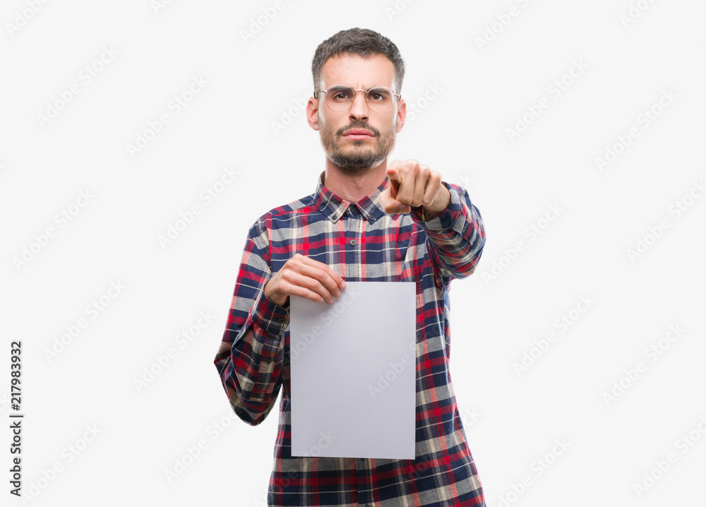 Young hipster adult man holding blank paper sheet pointing with finger to the camera and to you, hand sign, positive and confident gesture from the front Young hipster adult man holding blank paper sheet pointing with finger to the camera and to you, hand sign, positive and confident gesture from the front