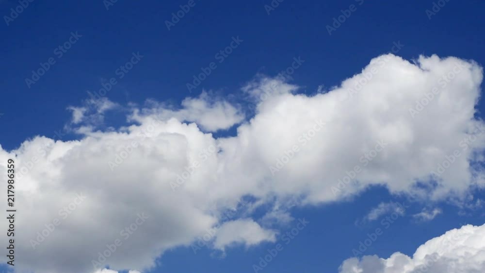 Puffy white clouds morph and roll across the frame against a brilliant blue sky. Puffy white clouds morph and roll across the frame against a brilliant blue sky.