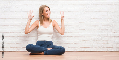 Beautiful young woman sitting on the floor at home showing and pointing up with fingers number eight while smiling confident and happy.