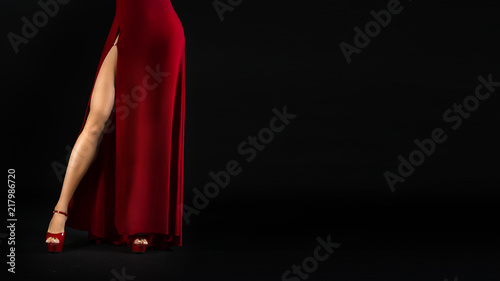 unrecognizable sexy female legs in a red dress and high heeled shoes on a black background.