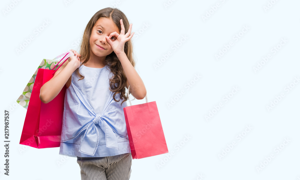 Brunette hispanic girl holding shopping bags with happy face smiling doing ok sign with hand on eye looking through fingers