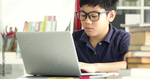 Asian teen boy waring eyeglass and used laptop computer at home, cute boy doing your homework with serious face.