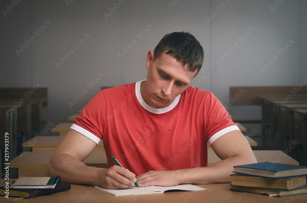 Serious student boy writing a lecture or exam work to the workbook. Serious student boy writing a lecture or exam work to the workbook.