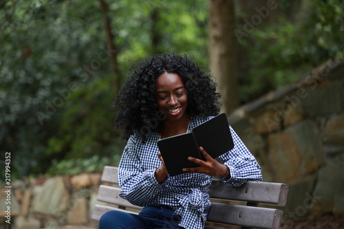 Smiling black woman reading electronic book on bench