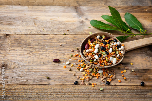Assortment of legumes in a ladle and spilled on a wooden tabletop background, copy space.