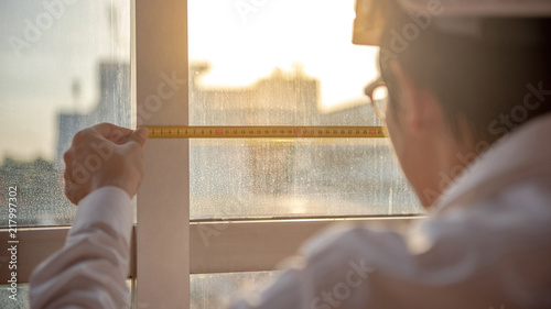 Young Asian engineer man using tape measure (measuring tape) on window frame at construction site, Length measurement tool or equipment for building construction working