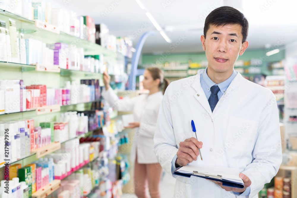 Chinese male is attentively looking medicine with notebook in apothecary
