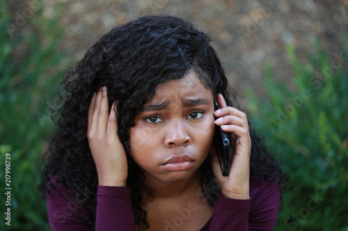 Upset black female touching hair and speaking on smartphone