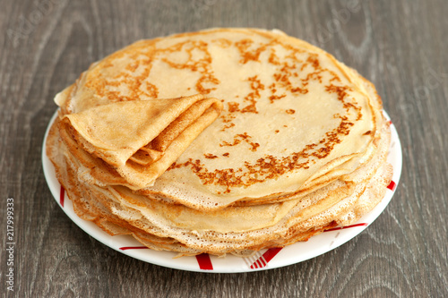 A stack of thin pancakes on a wooden background. Maslenitsa. Pancakes on a saucer close-up. Dessert for breakfast in the form of pancakes.