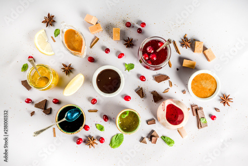 Various sweet sauces, toppings and syrups - lemon, orange, caramel, chocolate, cranberry, cherry, blueberry, on a light concrete background, top view copy space for text