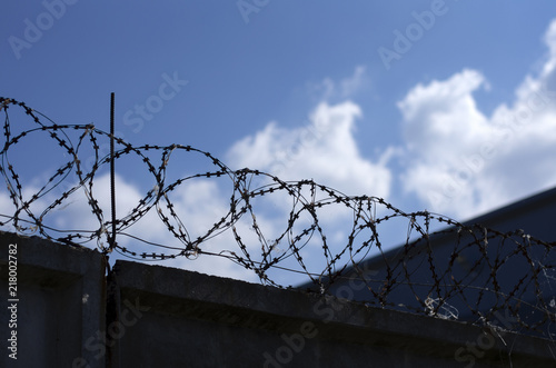Metal barbed wire over concrete fence against blue sky with clouds