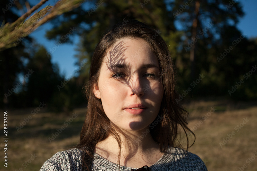 Pensive portrait of a charming girl with a shadow on her face from pine branches