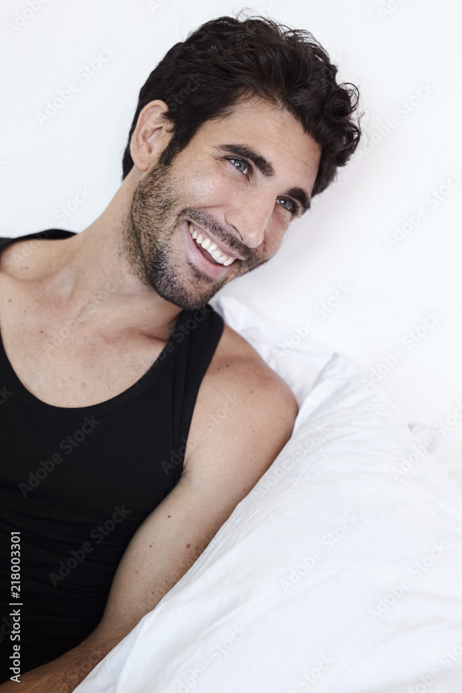 Laughing guy in bed wearing vest, looking away Laughing guy in bed wearing vest, looking away
