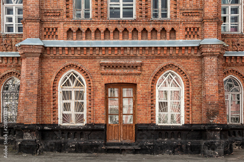 Close-up of a wooden porch with a brown door and old windows with an old house a mansion made of old brick