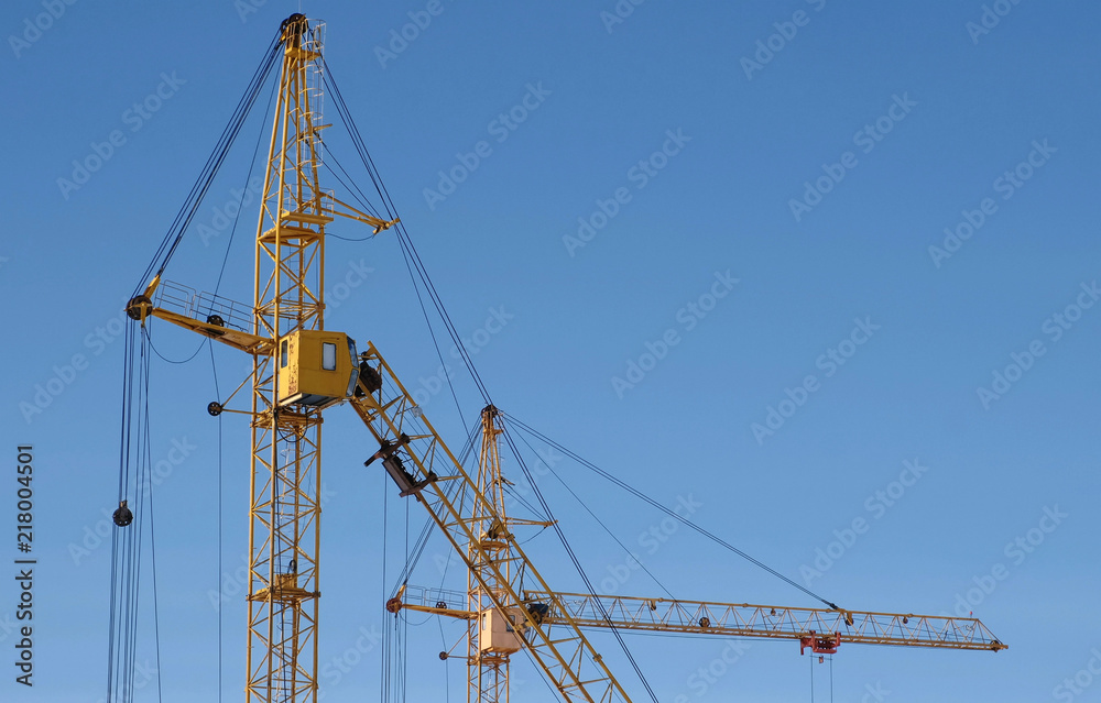 Two construction cranes against the sky background.