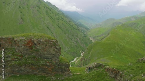 Woman walks in severe Ossetian mountains with revine on background covered with green grass photo