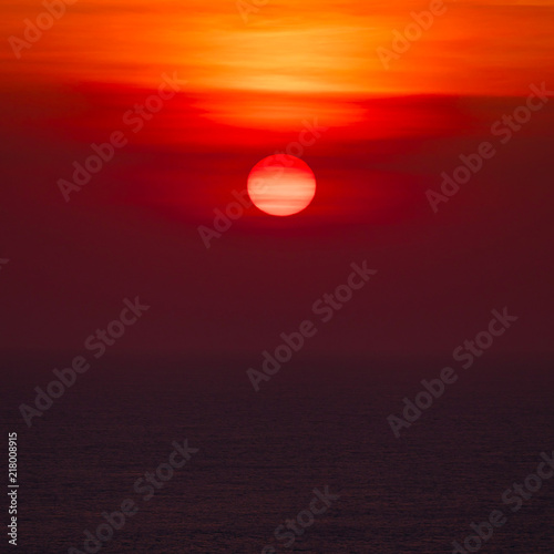 Sunset over ocean horizon photographed with big telephoto lens.