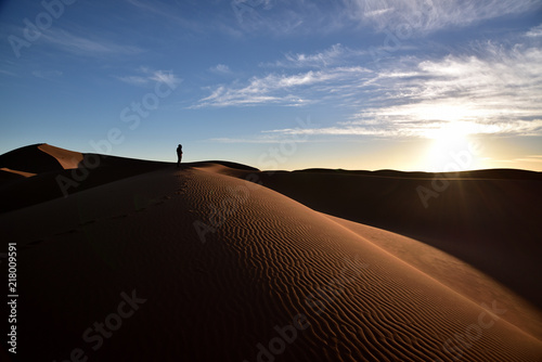 Eine Person steht auf der Düne und genießt den Sonnenuntergang
