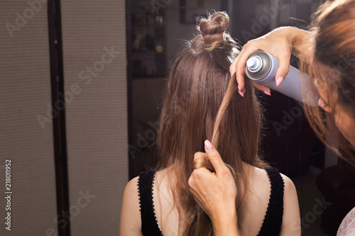 hairdresser fixing hairstrand of a young beautiful model with a coiffure using a hairspray in a beauty salon. concept of professional stylist studying