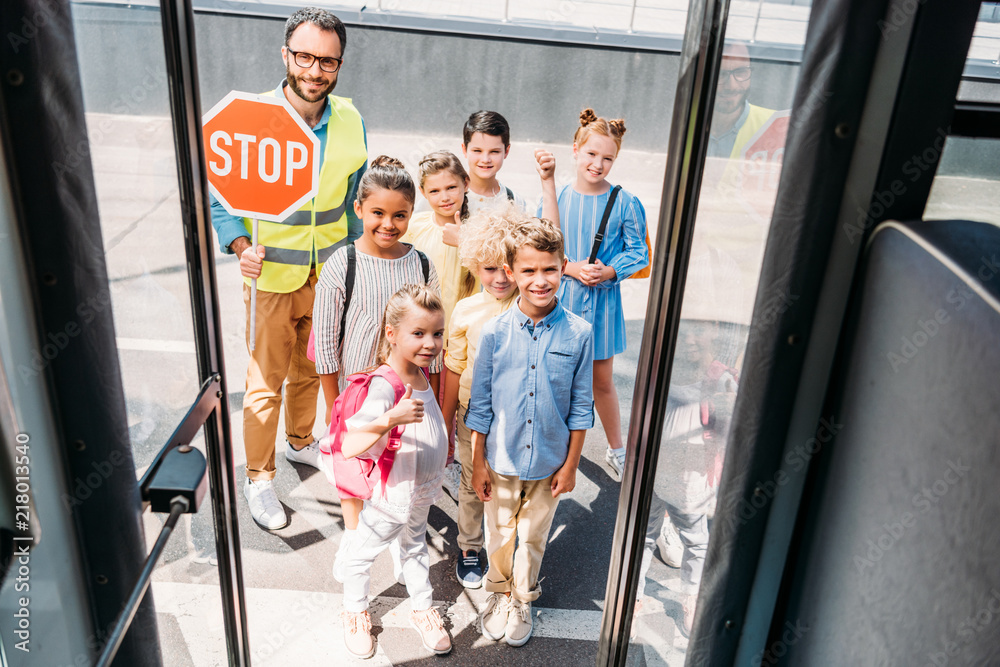 view from school bus at group of happy scholars with traffic guard looking at camera view from school bus at group of happy scholars with traffic guard looking at camera