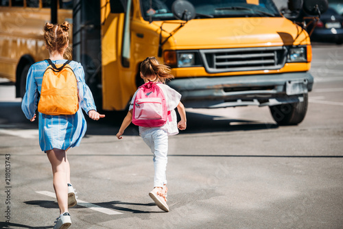 rear view of schoolgirls with backpacks running to school bus