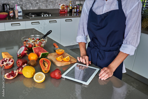 Woman looking at a recipe on her tablet as she stands in the kitchen in front of a table  with fresh ingredients