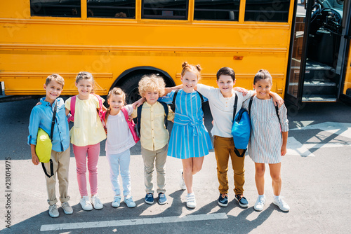 group of adorable schoolchildren standing in front of school bus and looking at camera
