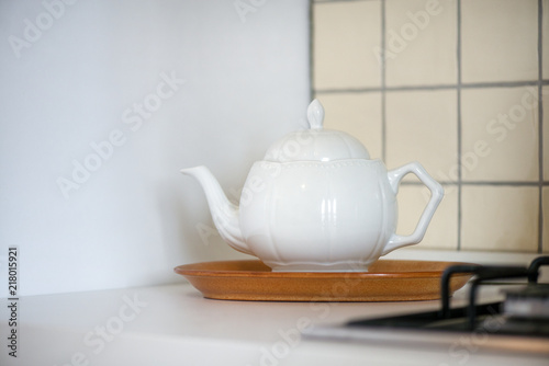 Modern clay tea pot next to an electric and gas stove in a kitchen