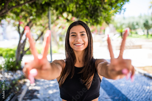 Happy beautiful latin girl show victory sign and smile. Urban scene, city life. photo