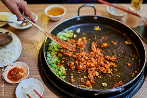 Korean spicy Kimchi bbq pork served on a hot pan with side dishes and rice as a background..