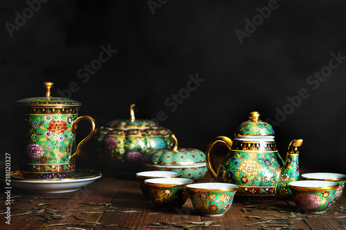 Still life of porcelain tea or coffee set of pot, jar cups and mug on wooden table with scrattered dry tea leaves on dark and smoky background photo