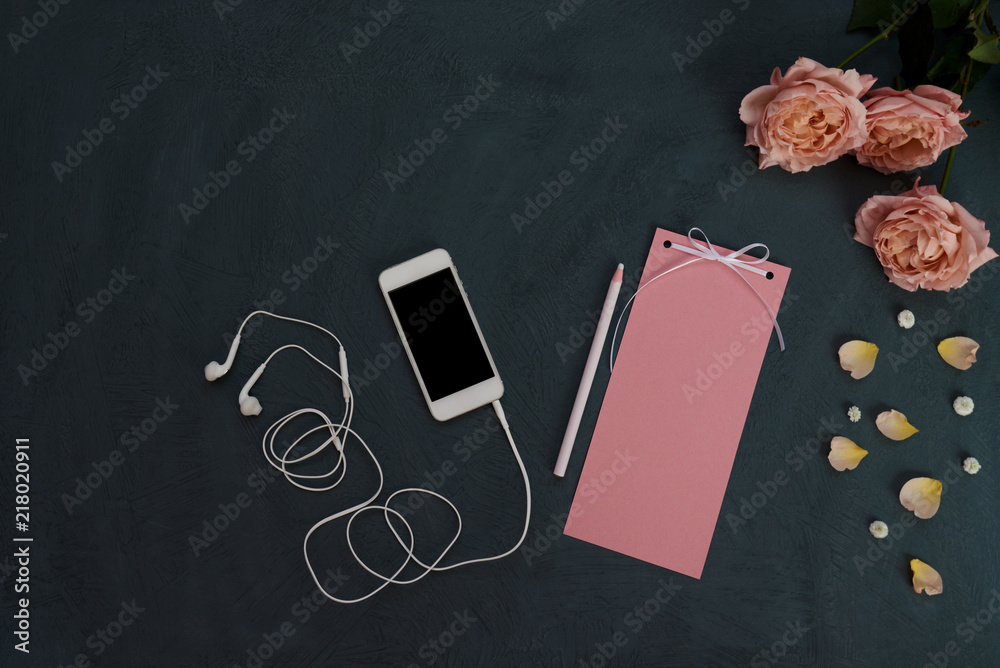Workspace with  smartphone, vintage paper for letter or message, pink petals and flowers on shabby blue background. Woman work desk for creativity. Still life of  items with pastel accents. Top view.