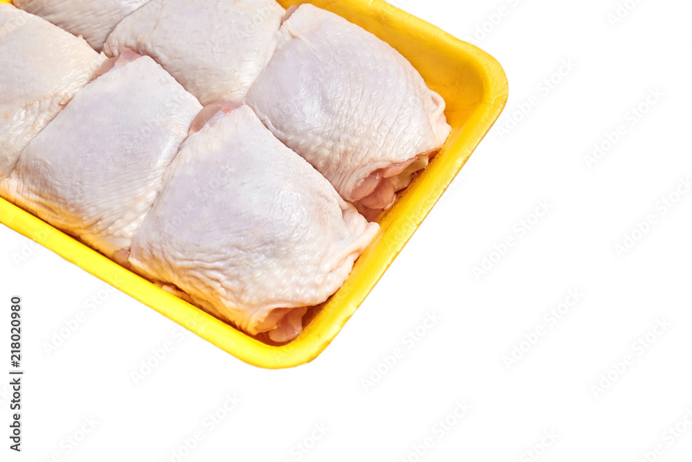 Raw and uncooked chicken thighs in a yellow plastic container. Meat of poultry in tray, isolated on white background
