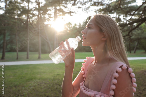 Beautiful young girl drinking water from a plastic bottle after a long walk in the woods