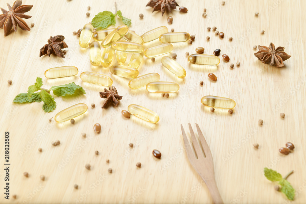 Medicine herb, Cod liver oil omega 3 gel capsules with healthy medicinal plant on wooden brown tone background with a wooden fork on foreground. Medicine herb, Cod liver oil omega 3 gel capsules with healthy medicinal plant on wooden brown tone background with a wooden fork on foreground.