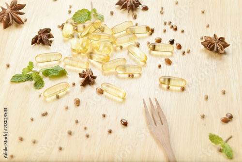 Medicine herb, Cod liver oil omega 3 gel capsules with healthy medicinal plant on wooden brown tone background with a wooden fork on foreground.